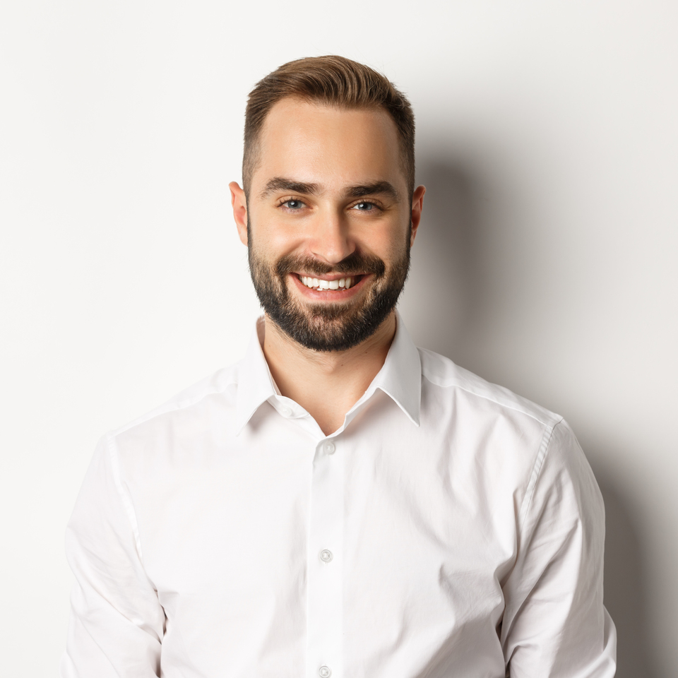 Close-up of confident male employee in white collar shirt smiling at camera, standing self-assured against studio background